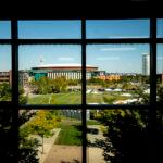 Ball arena can be seen through the silhouetted grid of a window in the foreground, surrounded by blue skies and green lawns.