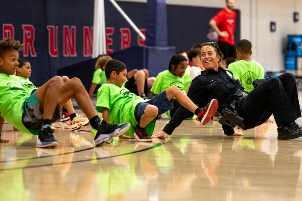 A woman dressed in a black police uniform crawls on her hands and feet — belly up, kind of like a crab — along with a bunch of kids in lime-green t-shirts. They're all beaming.