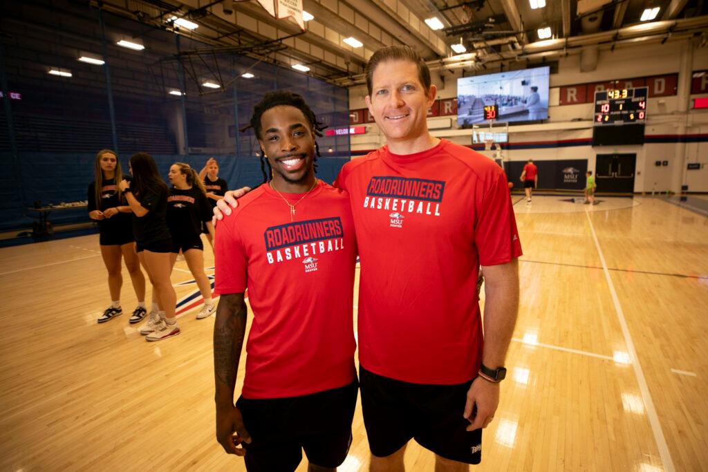 Two men in red shirts reading "ROADRUNNERS BASKETBALL" Stand arm in arm and smile at the camera. They are standing on a basketball court.