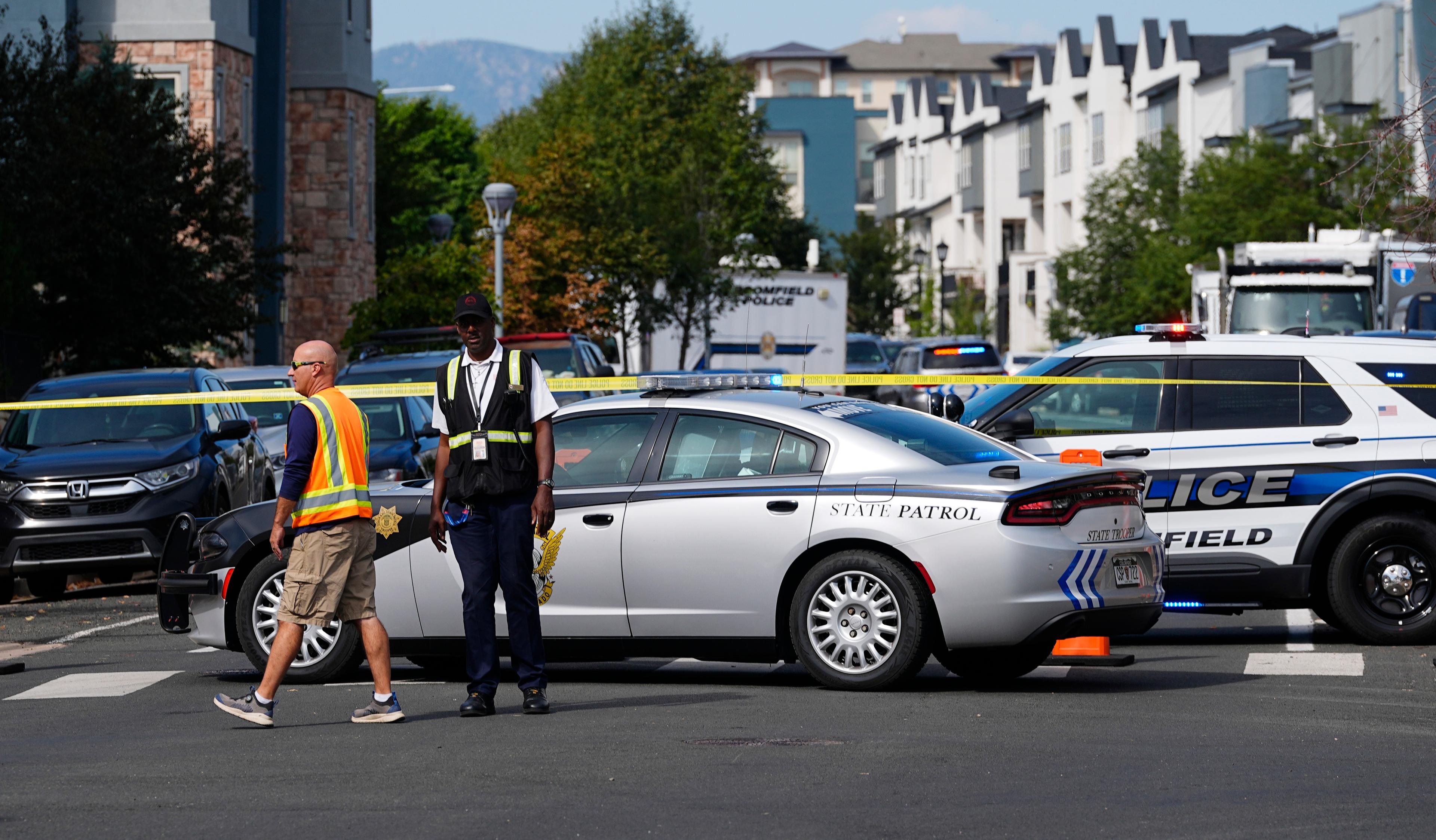 Two men stand in front of police tape outdoors.