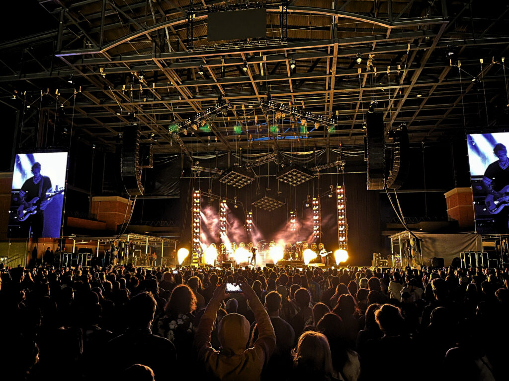 Fans pack the floor for Cage the Elephant. The sky is dark and the stage light illuminates the tops of people's heads.