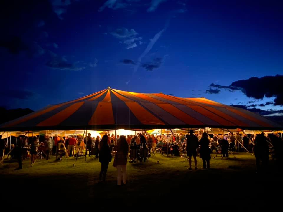 Lights glow from beneath the big tent at night as people crowd in to watch the show