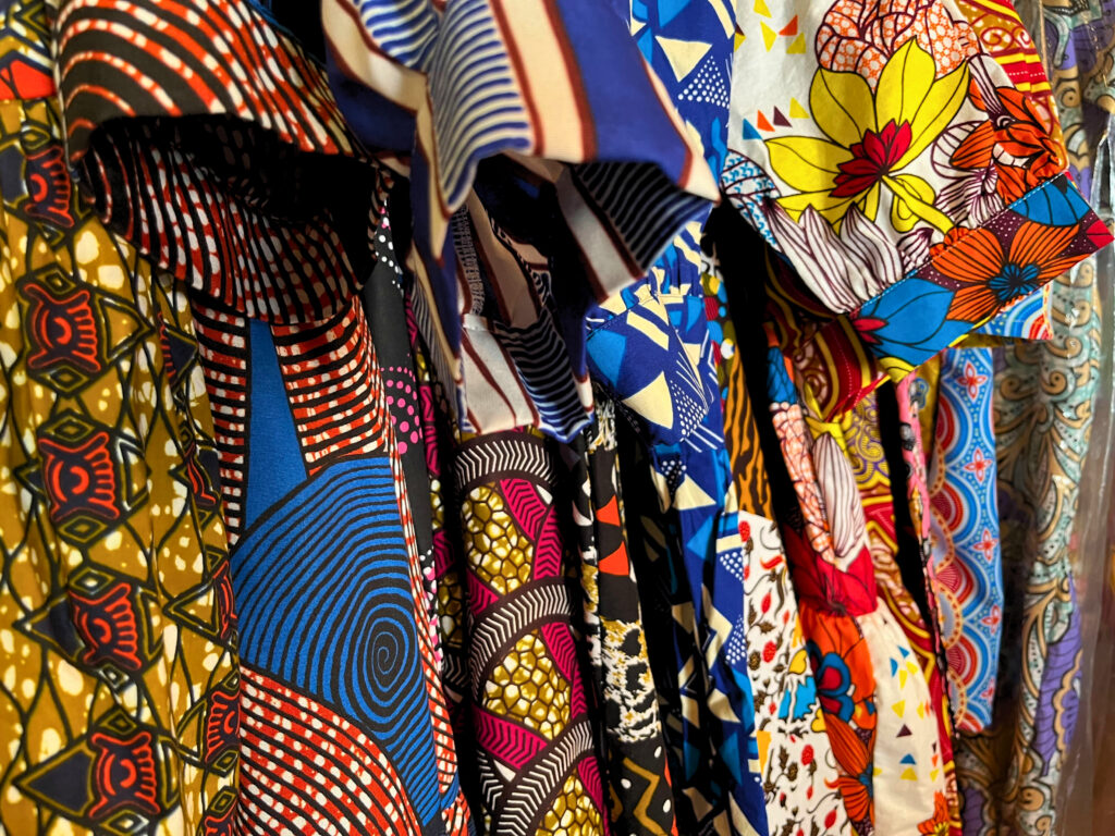 OULA garments on a rack in founder Erika Dalya Massaquoi's home. They are all vibrant with large patterns, mostly in blues, reds, whites and yellows.