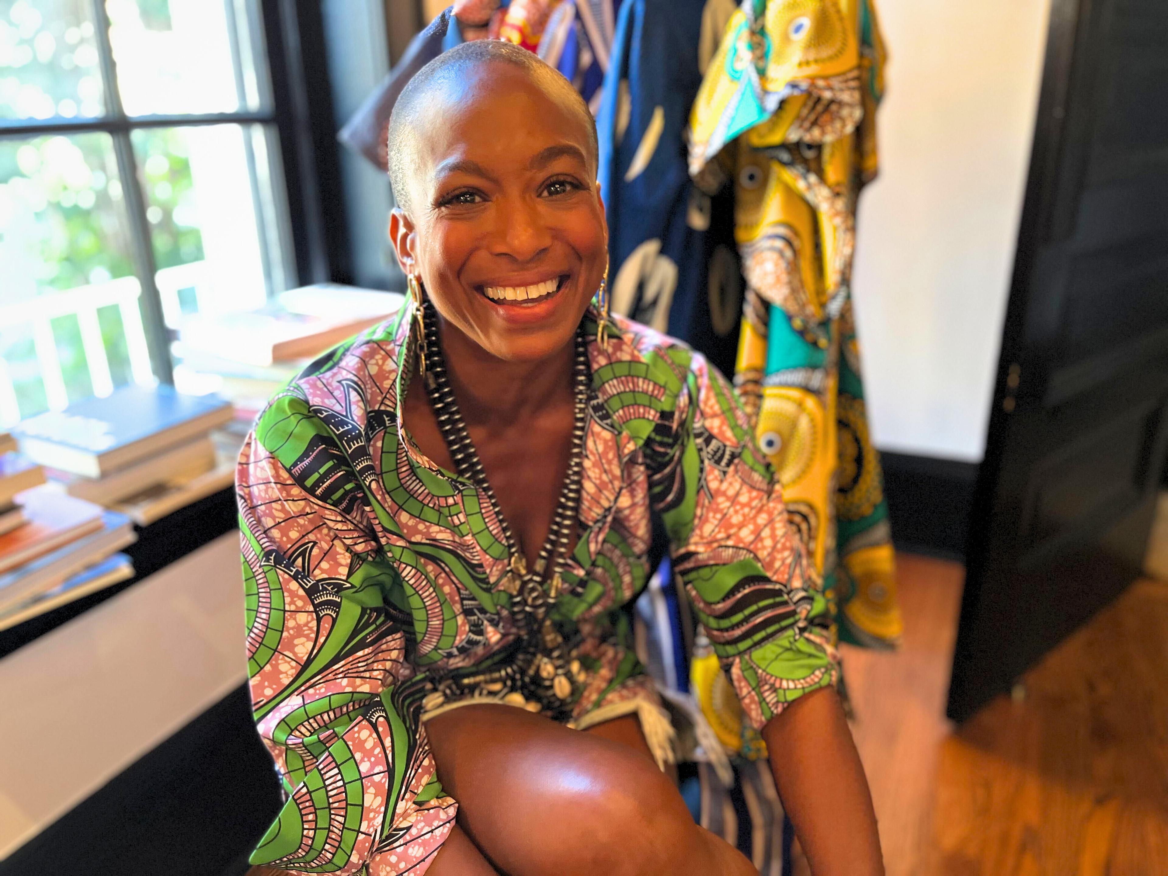 Erika Dalya Massaquoi, founder of OULA, smiles and leans towards the camera in one of her pink and green blouses.