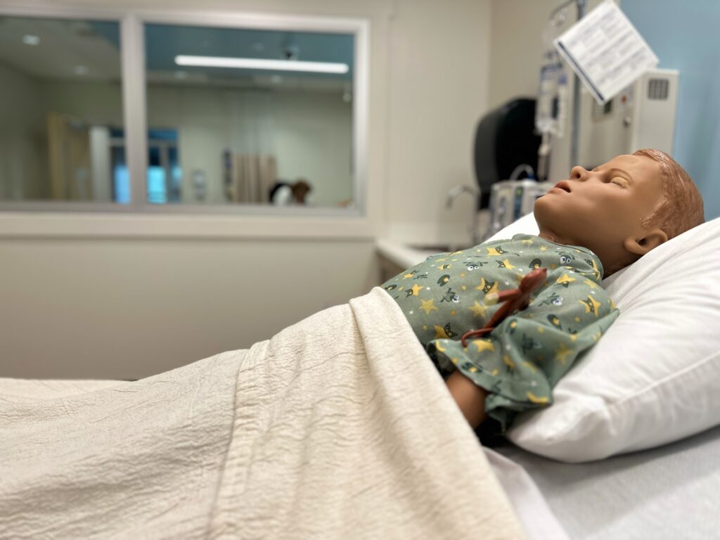 A pediatric mannequin in a hospital bed.