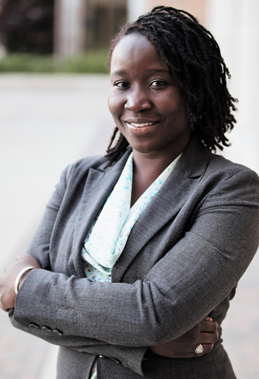 Ndeye Ndao is the Treasurer and Advisor for Refugees + Immigrants United. In this photo she stands, smiling at the camera in a suit jacket and blouse.