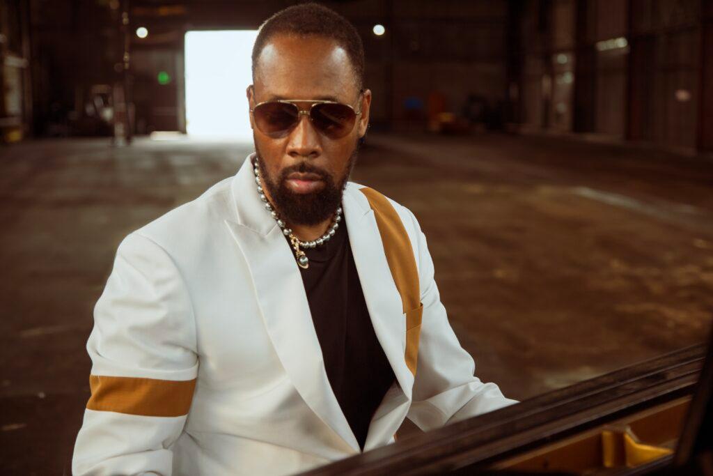 RZA wearing a white suit seated at a piano in a performance warehouse