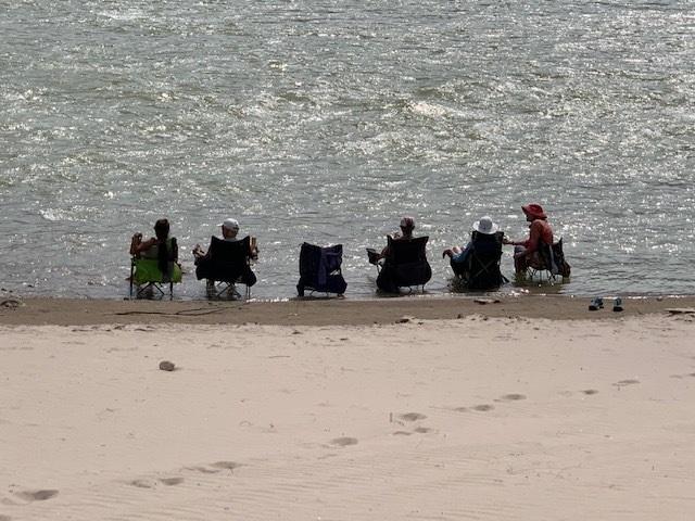 Five women sit in folder chairs on the bank of the Colorado River.