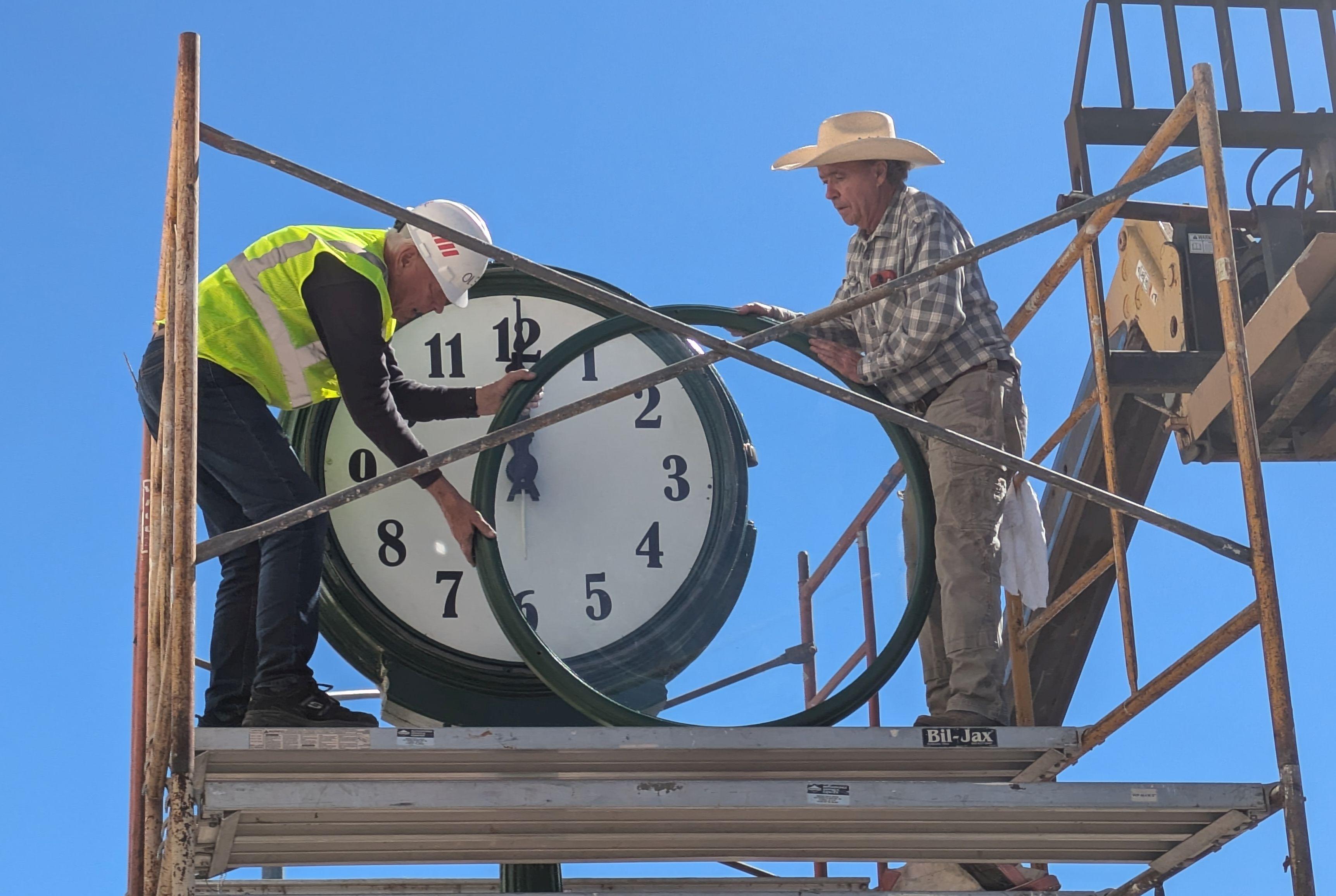 Two workers stand on scaffolding putting the rim on to a large clock face