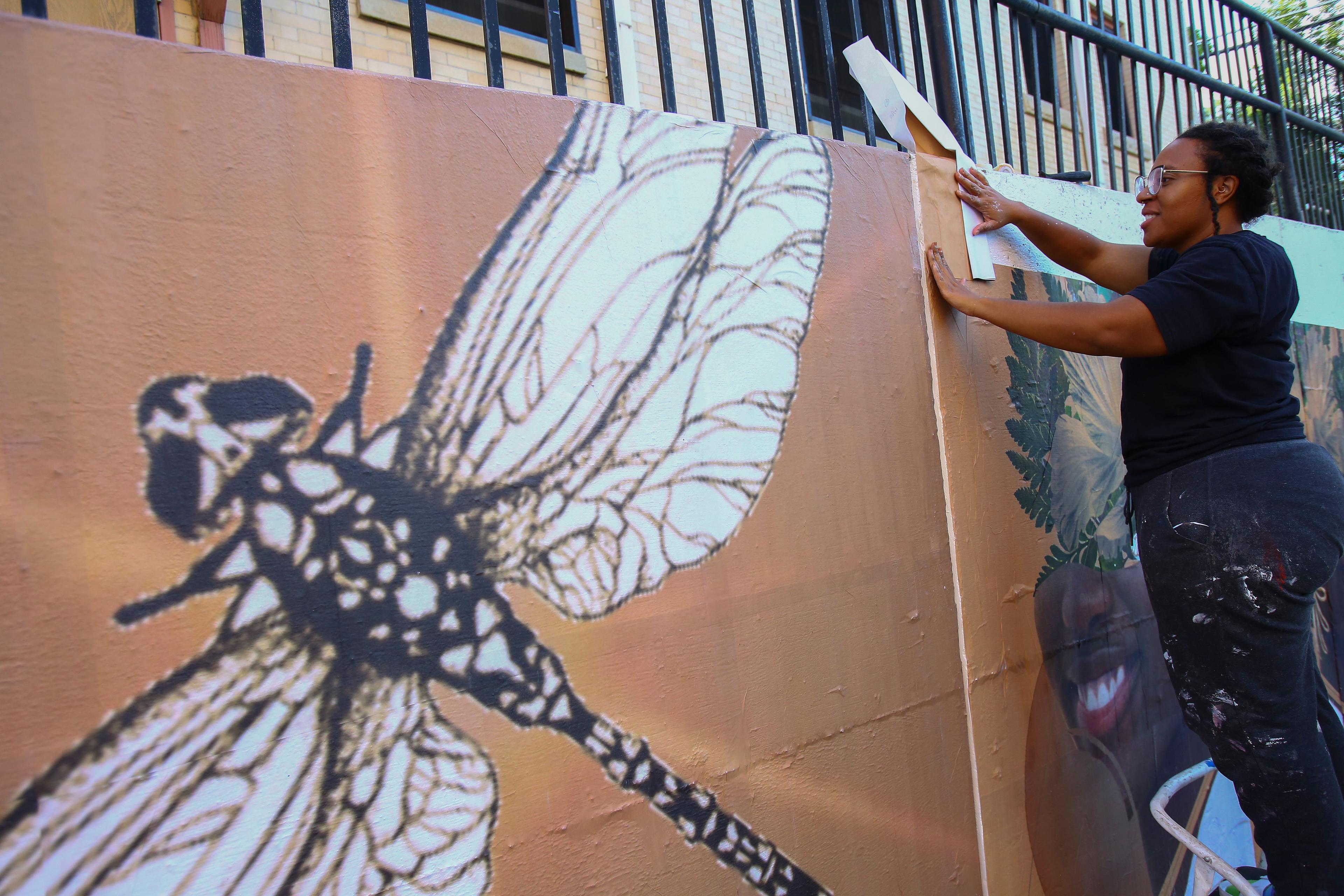 Artist Yazmin Atmore at work on a mural in Boulder with a large image of a dragonfly in the foreground