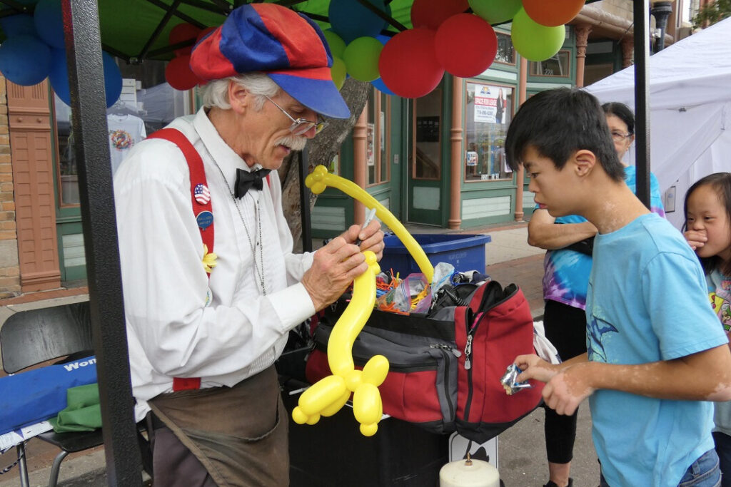 A man makes a yellow balloon animal as a child looks on