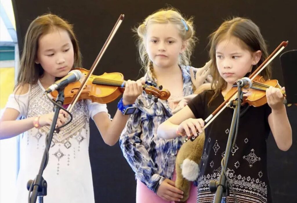 Three young children perform, two of them playing fiddles, perform as part of the bluegrass festiival