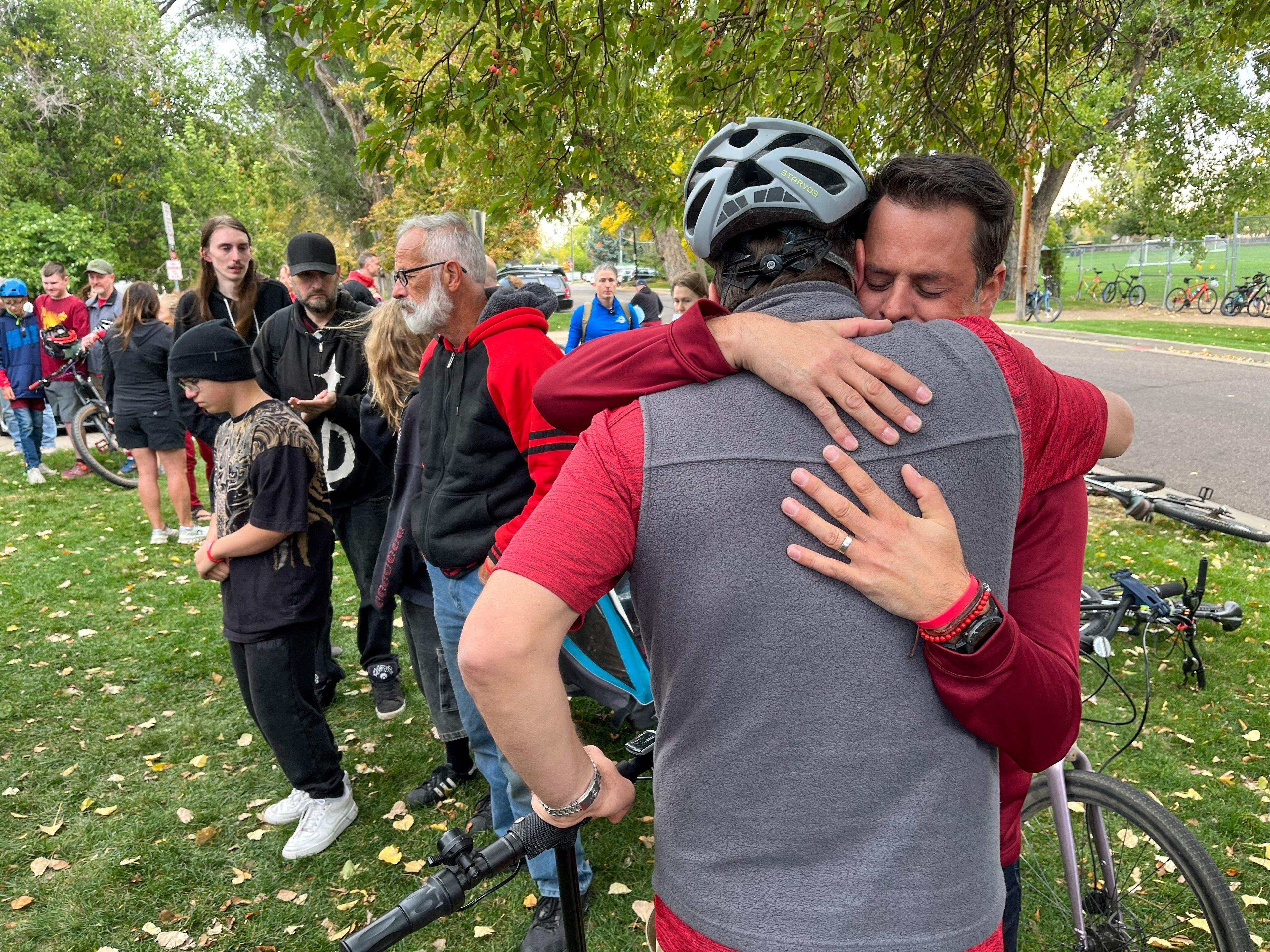 A father closes his eyes while his friend hugs at a memorial for his son