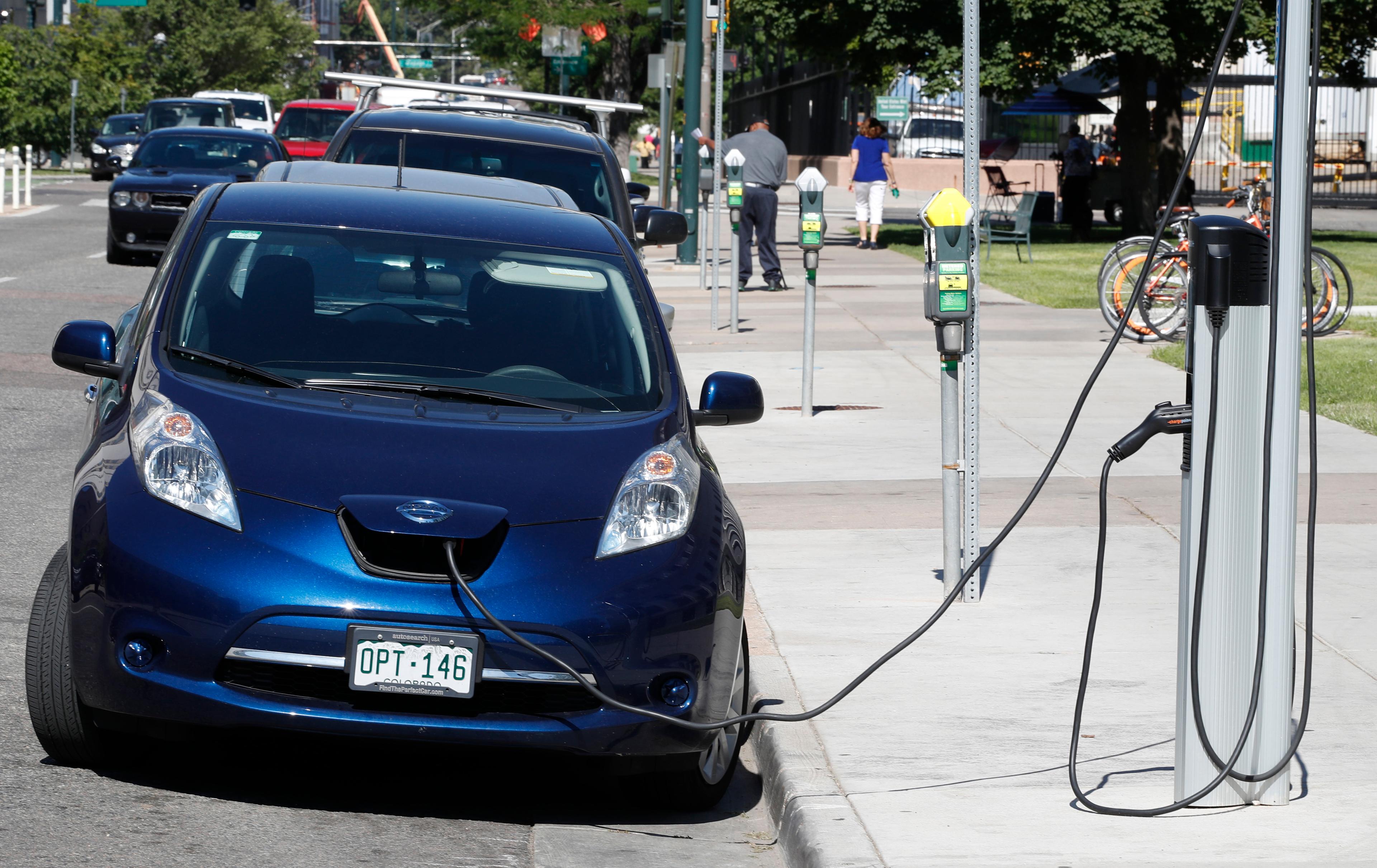 A blue car is plugged into a station on a street and viewed from the front.