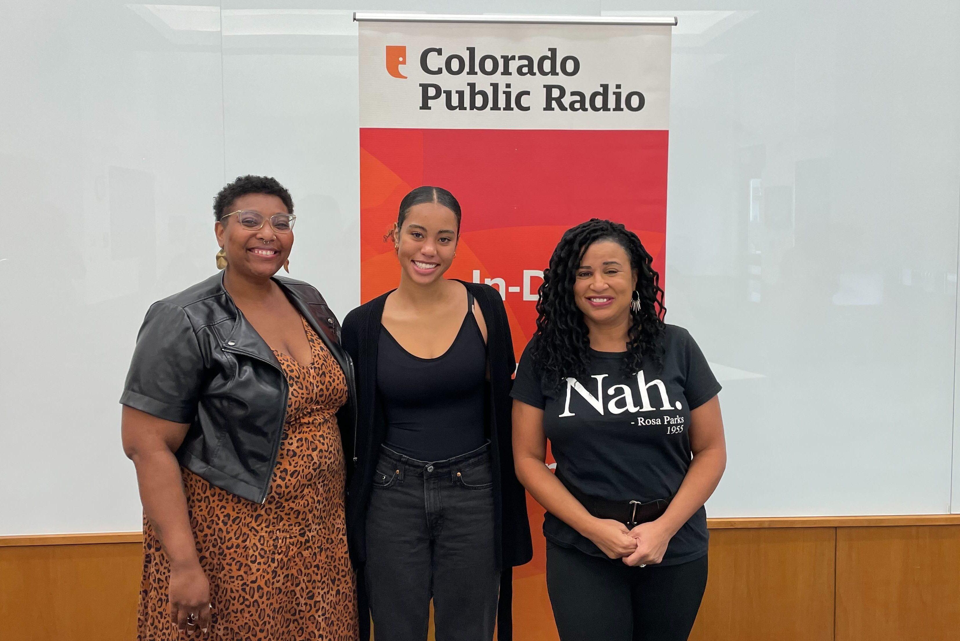 Author Evette Dionne stands next to Manual High School student Jaci Colllins-Falcon and Colorado Matters host Chandra Thomas Whitfield in front of a CPR News sign at an event at the Blair Caldwell African-American Research Library in Denver.