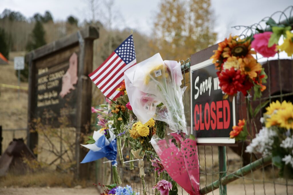 Memorial flowers are hung on a closed gate.