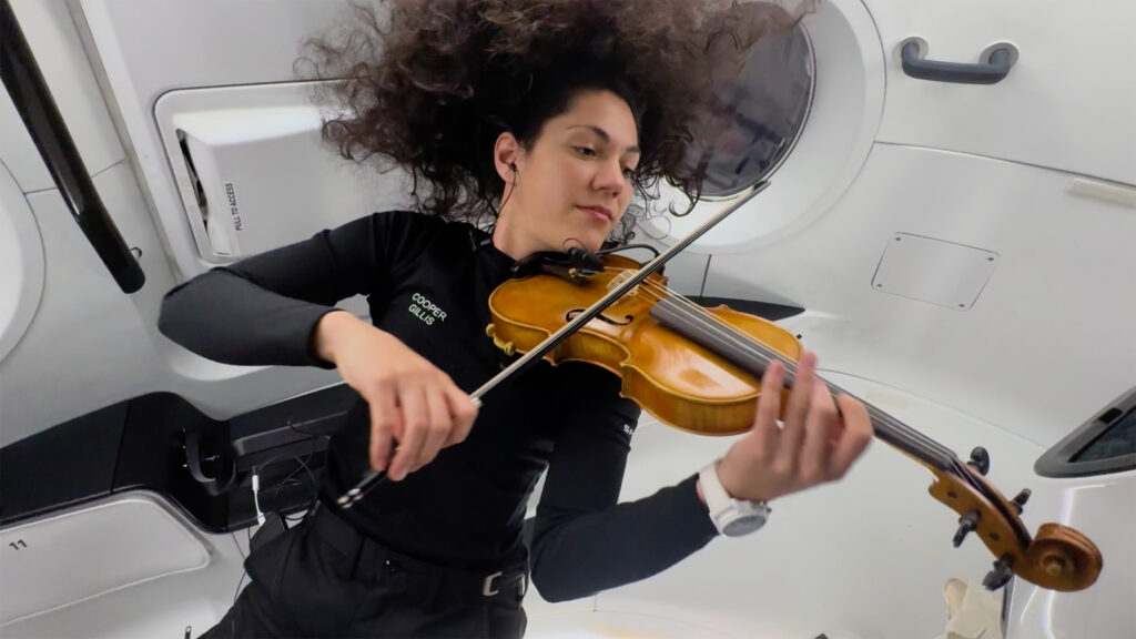 Astronaut Sarah Gillis is pictured playing the violin inside the Crew Dragon space capsule. She played with a group of young musicians on Earth.