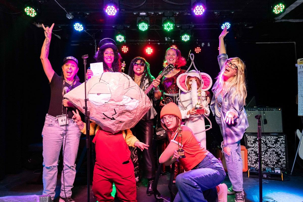 Eight people wearing costumes stand on stage and pose for the camera