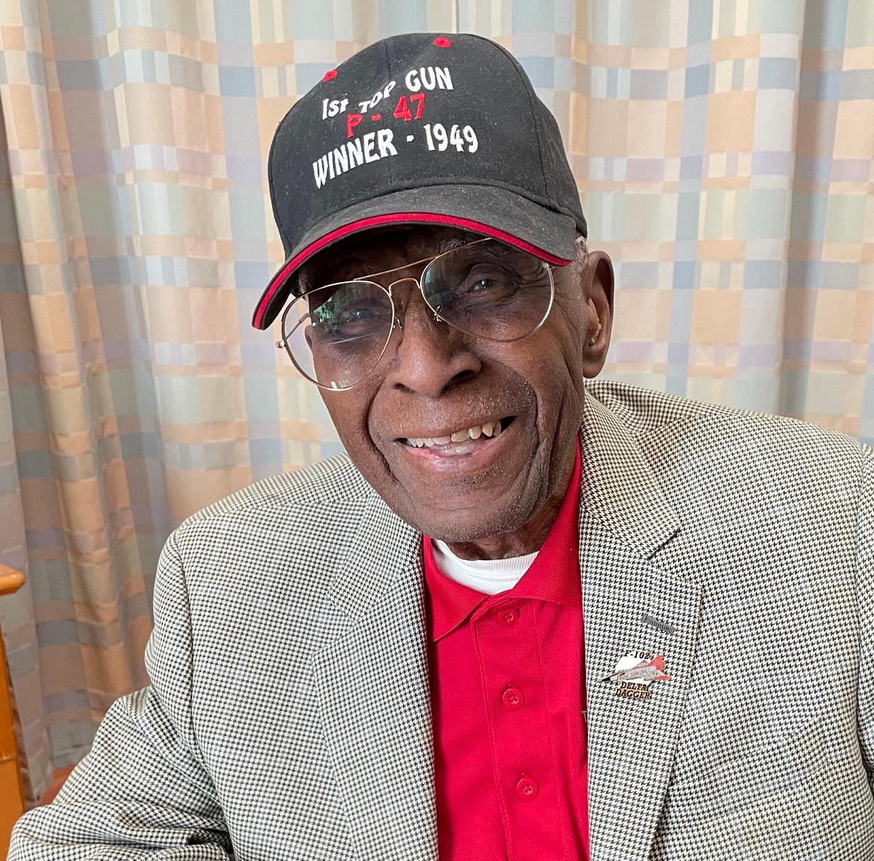 Colonel James Harvey, 101, sits with a baseball cap that identifies his Tuskegee team as winners of the first-ever Top Gun competion in 1949.