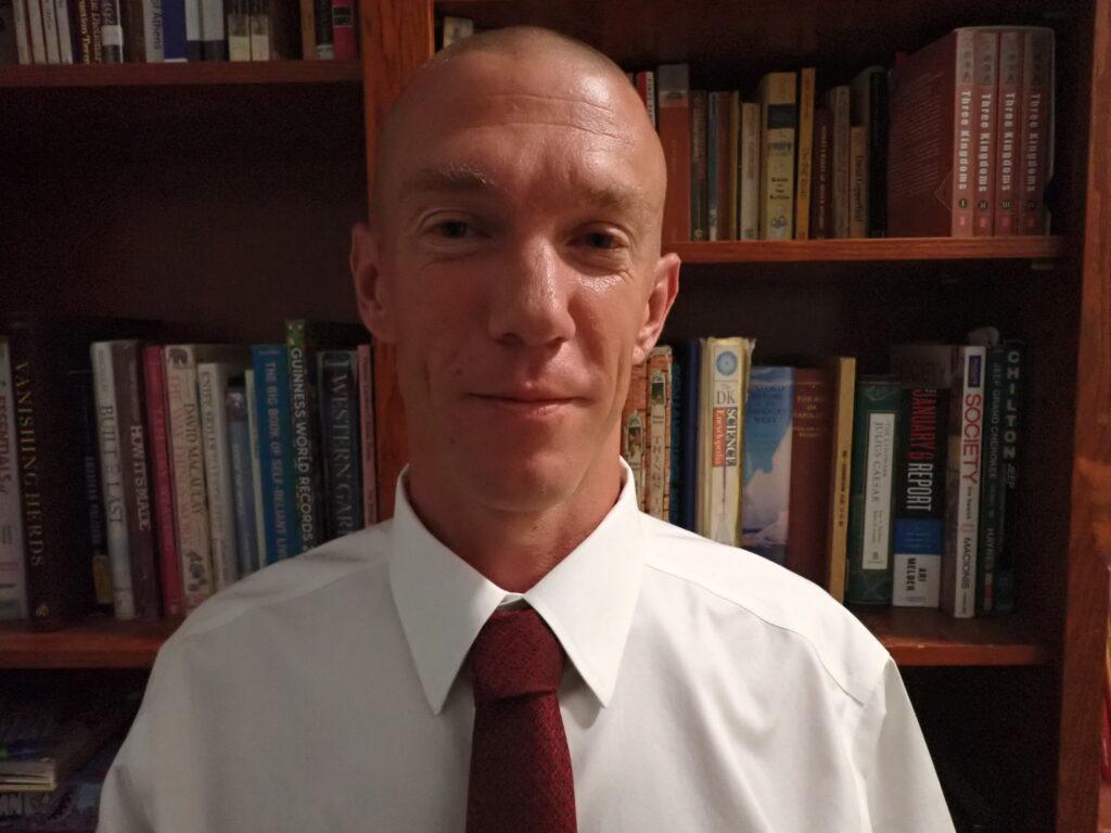 A head shot of Adam Withrow. Withrow is wearing a white dress shirt with a red tie.