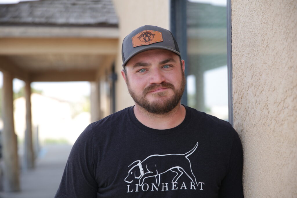 A man with a gray ballcap wears a black t-shirt with a picture of a hunting hound on it.