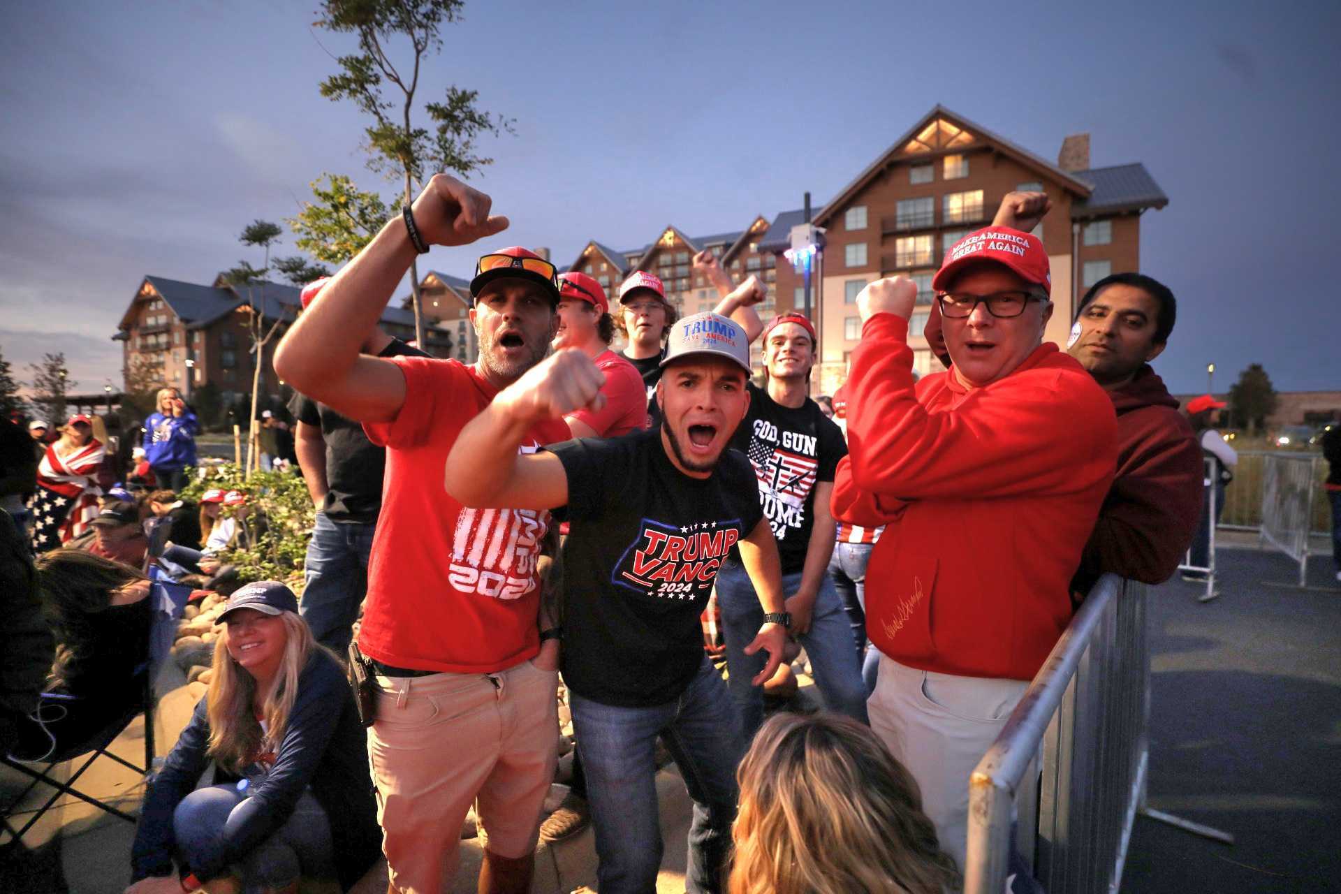 A group of enthusiastic men in Trump/Vance gear cheer for the camera with the Gaylord Rockies building behind them.