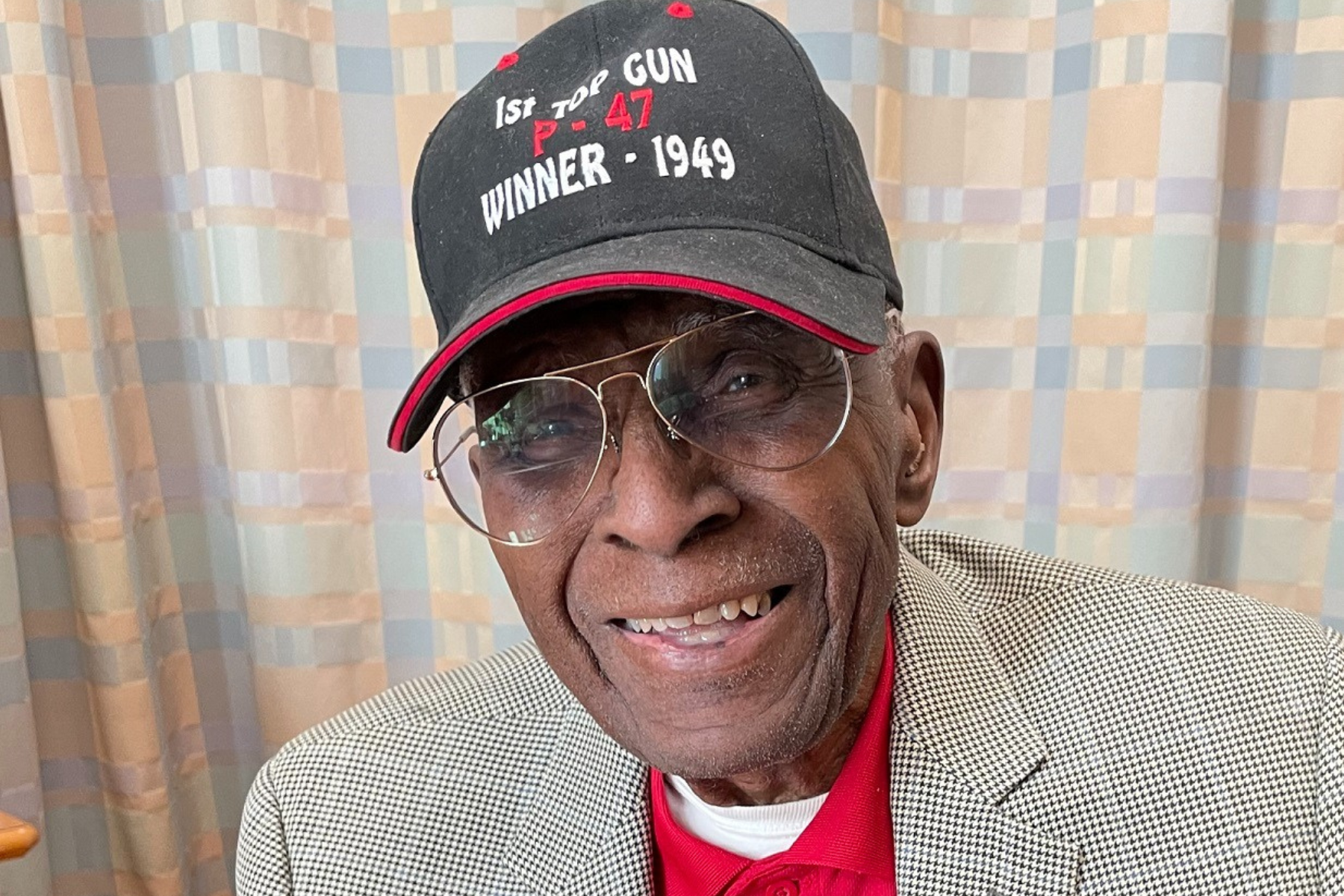 Colonel James Harvey, 101, sits with a baseball cap that identifies his Tuskegee team as winners of the first-ever Top Gun completion in 1949.