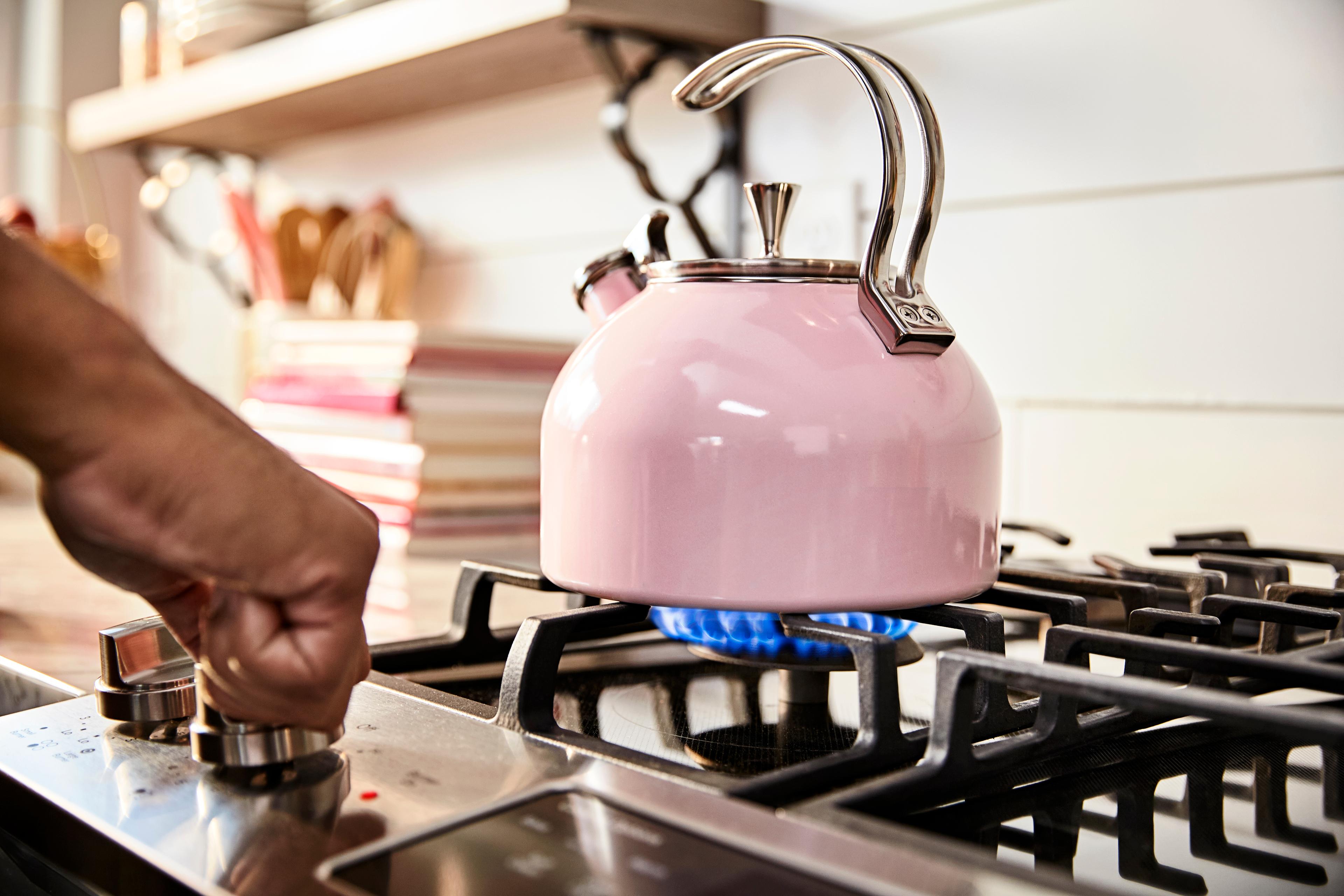 a person heats water in a pink tea kettle on a gas burner