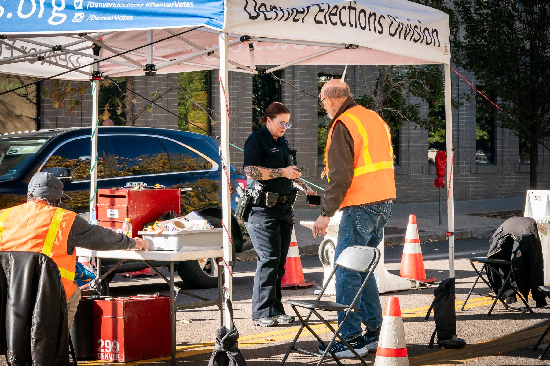 Denver police officer provides security with Denver Elections Division ballot drop-off workers