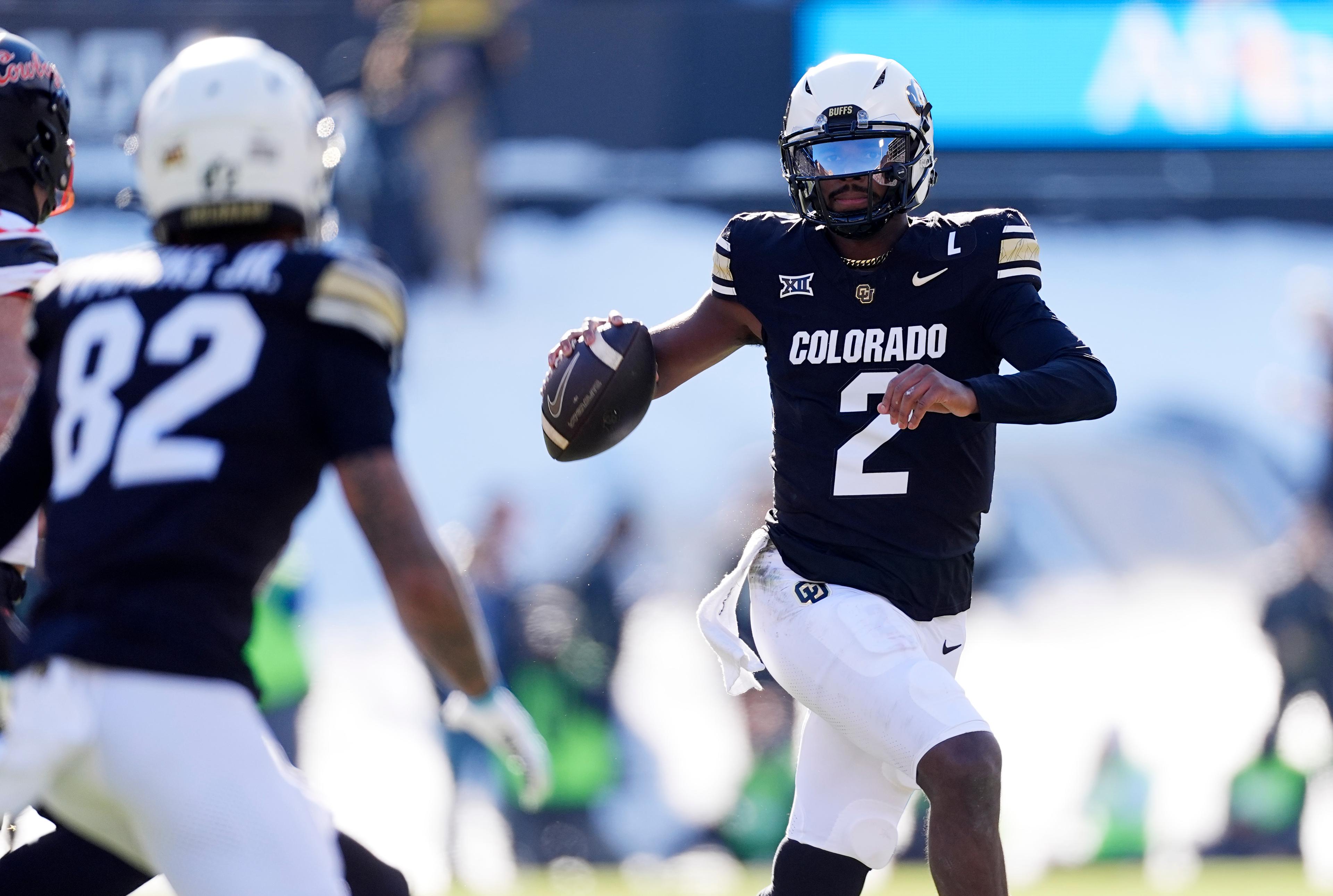 A man in a black jersey gets ready to throw a football with a receiver in the foreground.