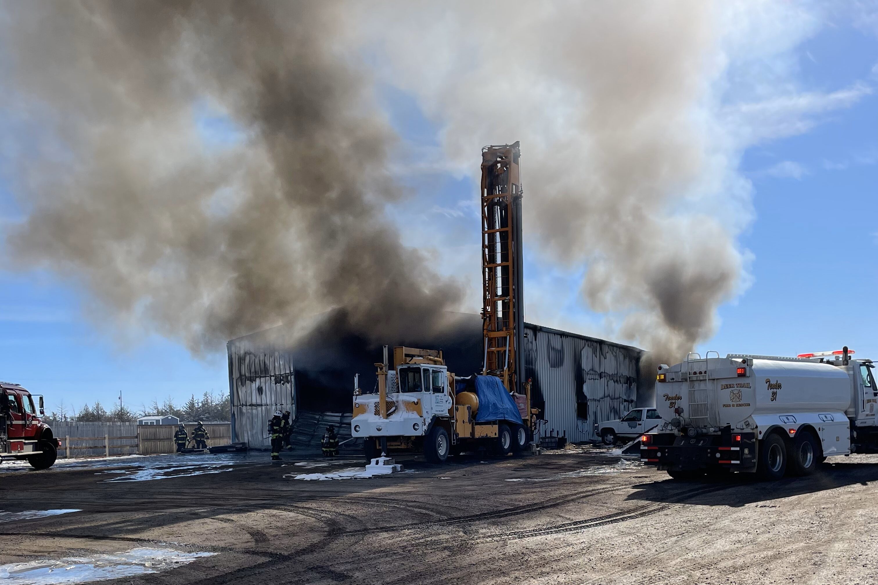 Smoke pours out of a large building on fire with vehicles around it.