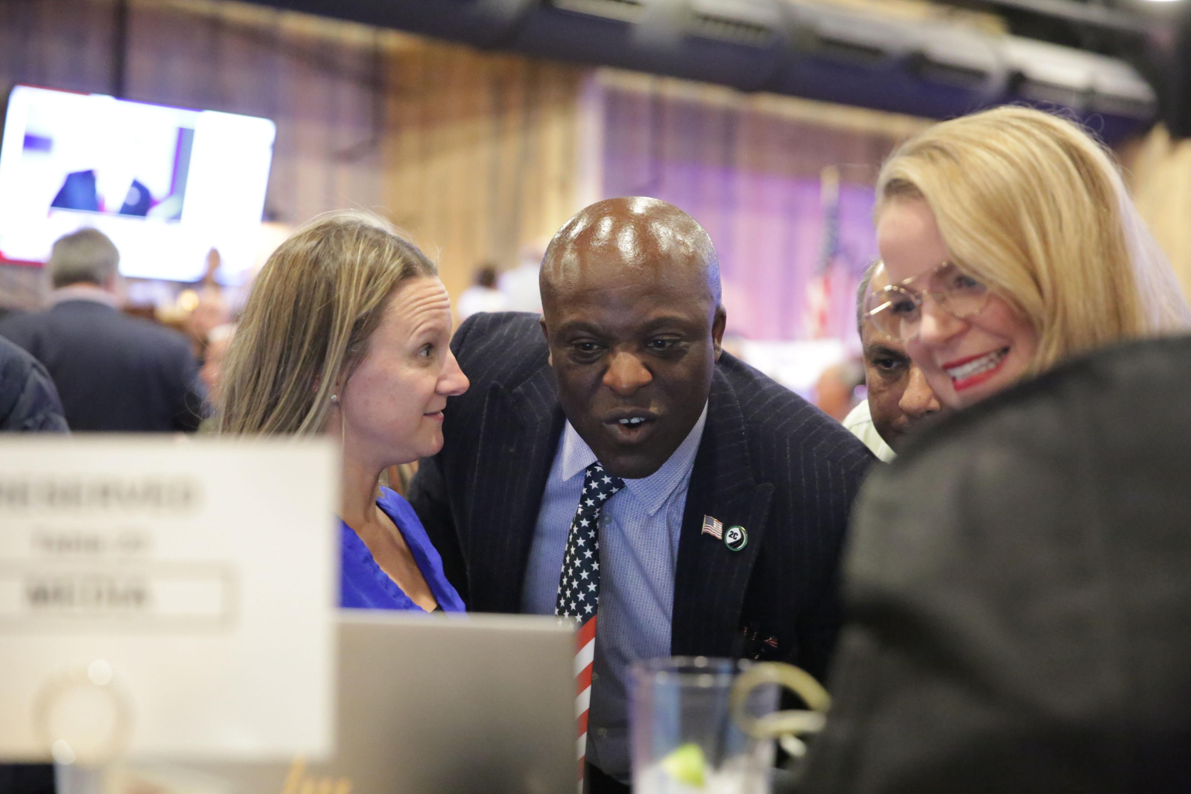 A group of people stand around a laptop, looking at election results.