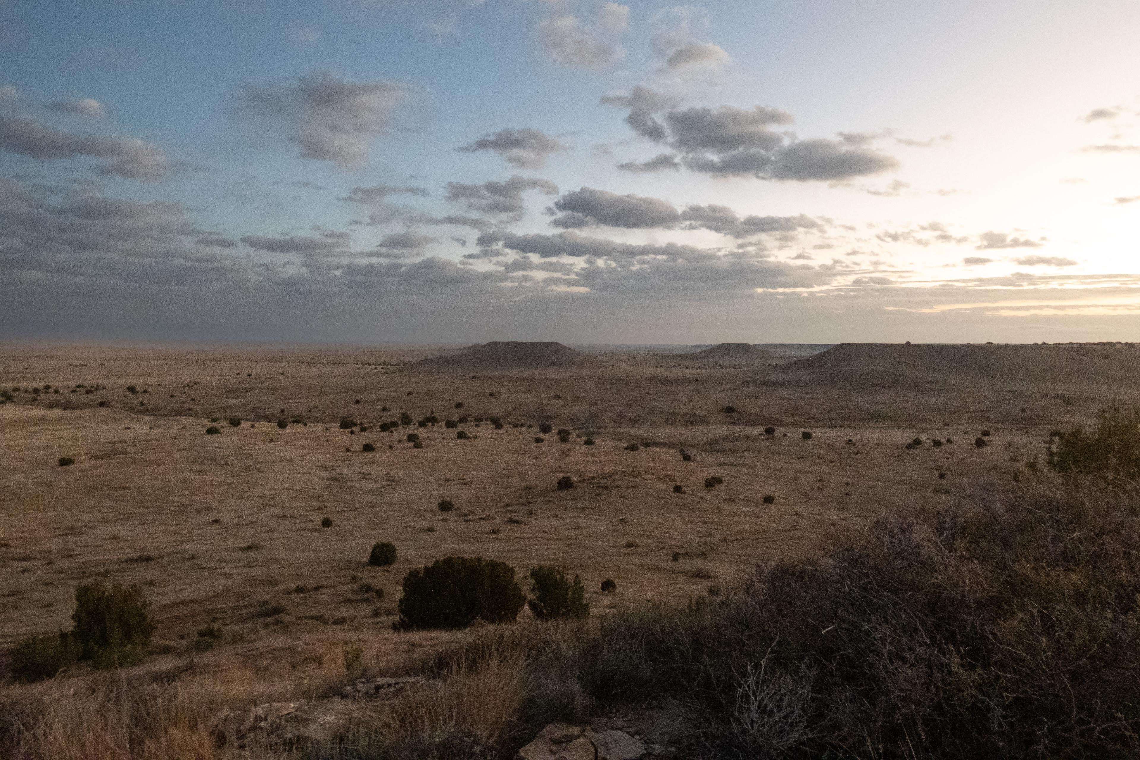 a vast view of the prairie at sunrise with several mesa land formations in the distance