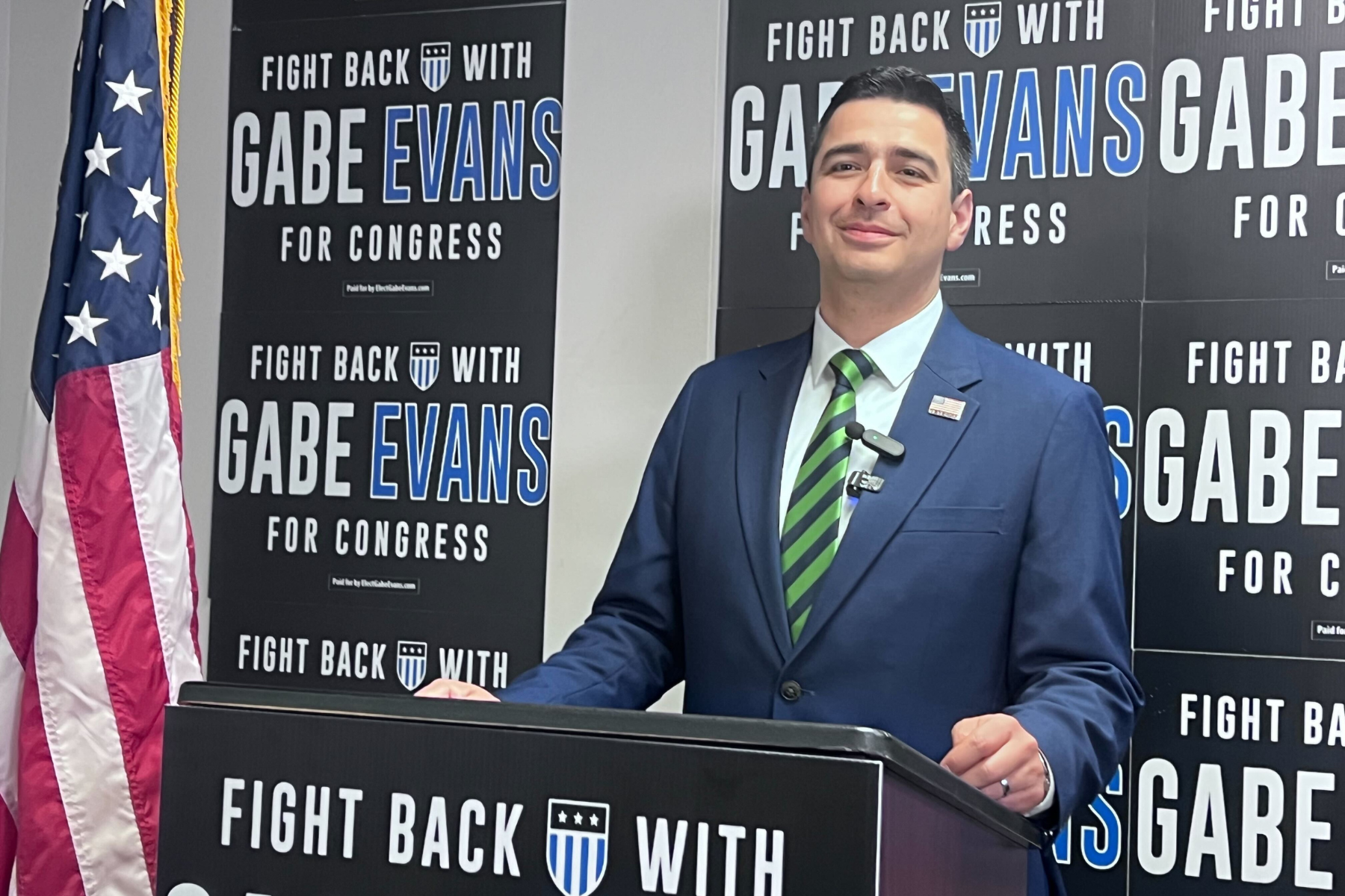 Gabe Evans standing in front of a wall brandished with his campaign signs