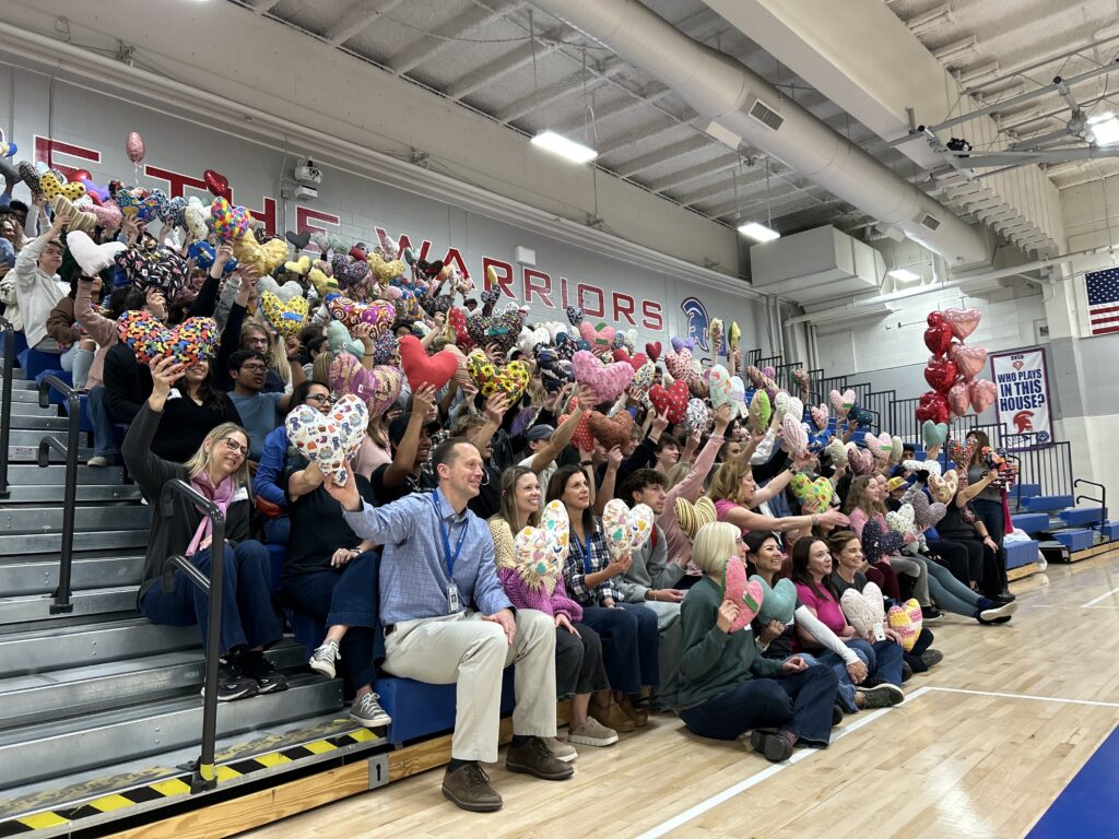 Centaurus high school students and faculty sit on the gym bleachers and hold up more than 400 heart-shaped pillows.