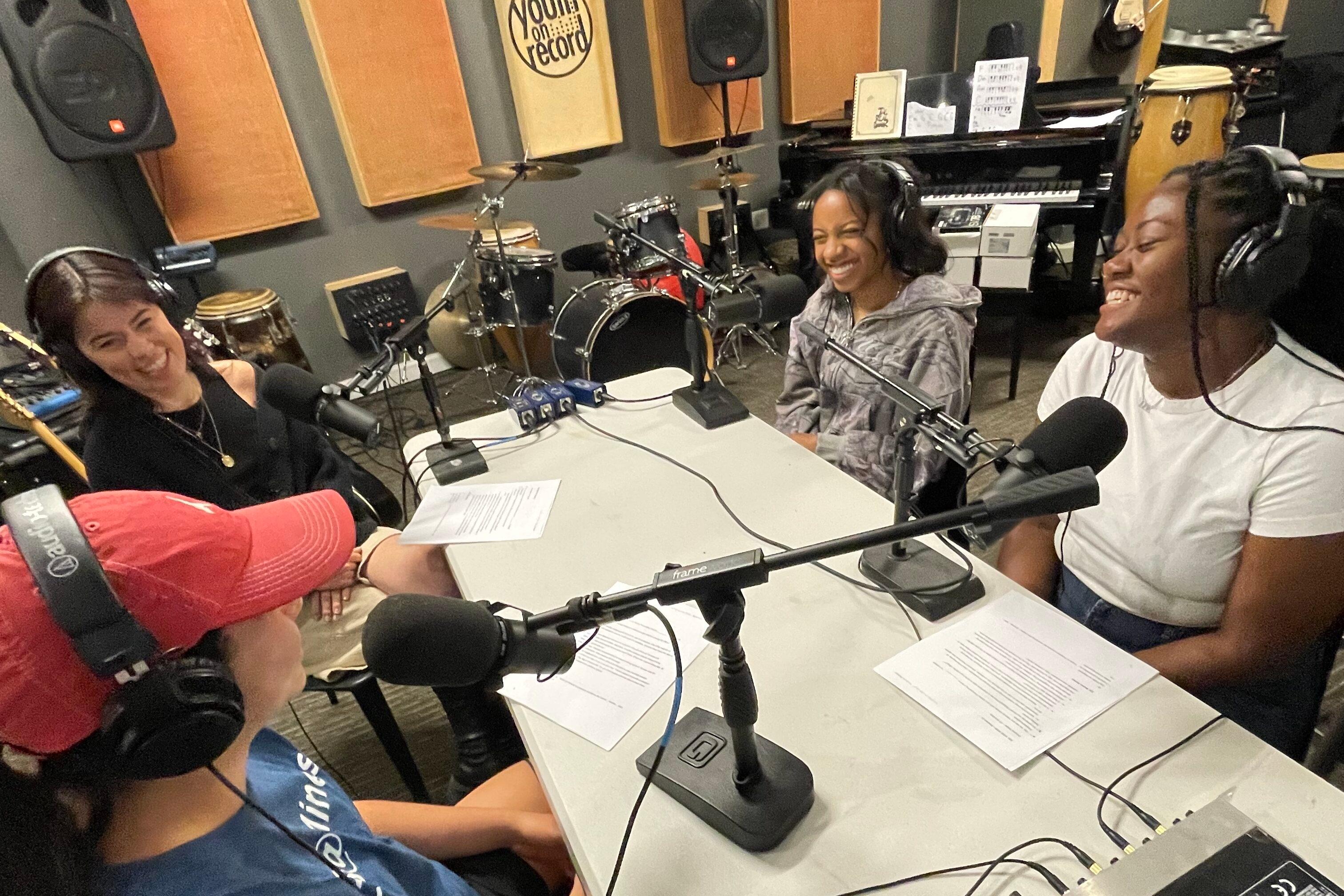 Four participants in Youth on Record are seated in front of microphones at a table in a recording stucio.