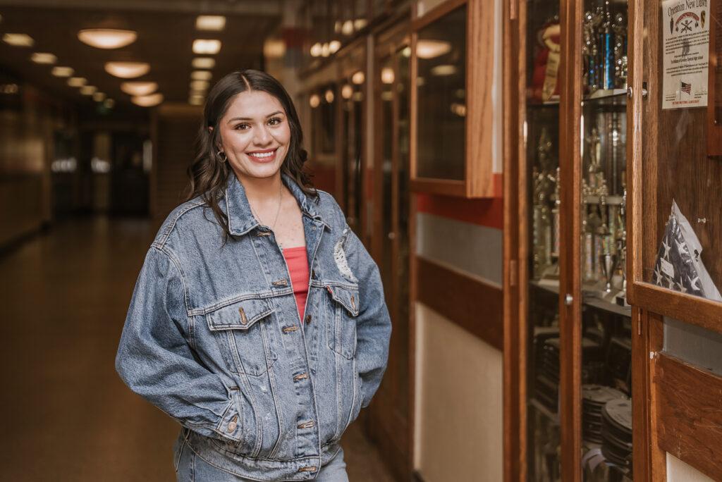 A high schooler stands in a hallway near a case with trophies.