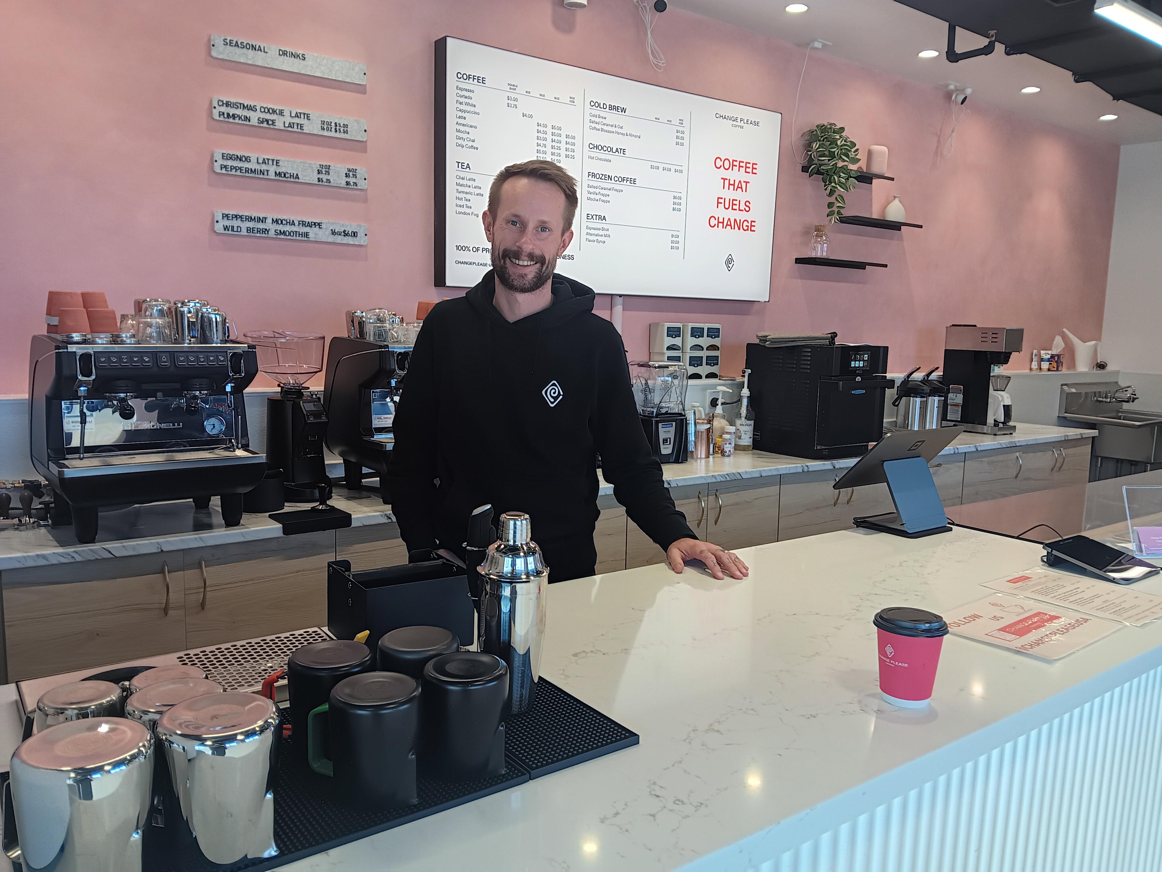 slender young-to-middle aged man standing behind counter in coffee shop