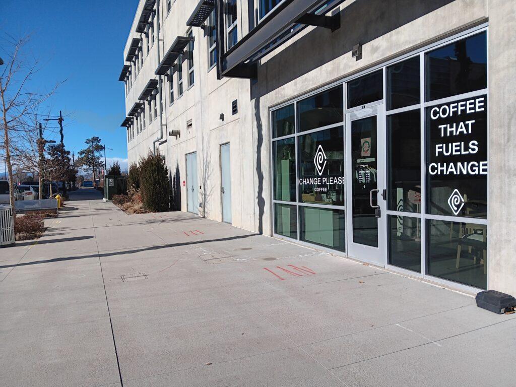 image of a cement sidewalk on the left, and on the right the glass storefront of a coffee shop with white lettering on it that says Coffee That Fuels Change