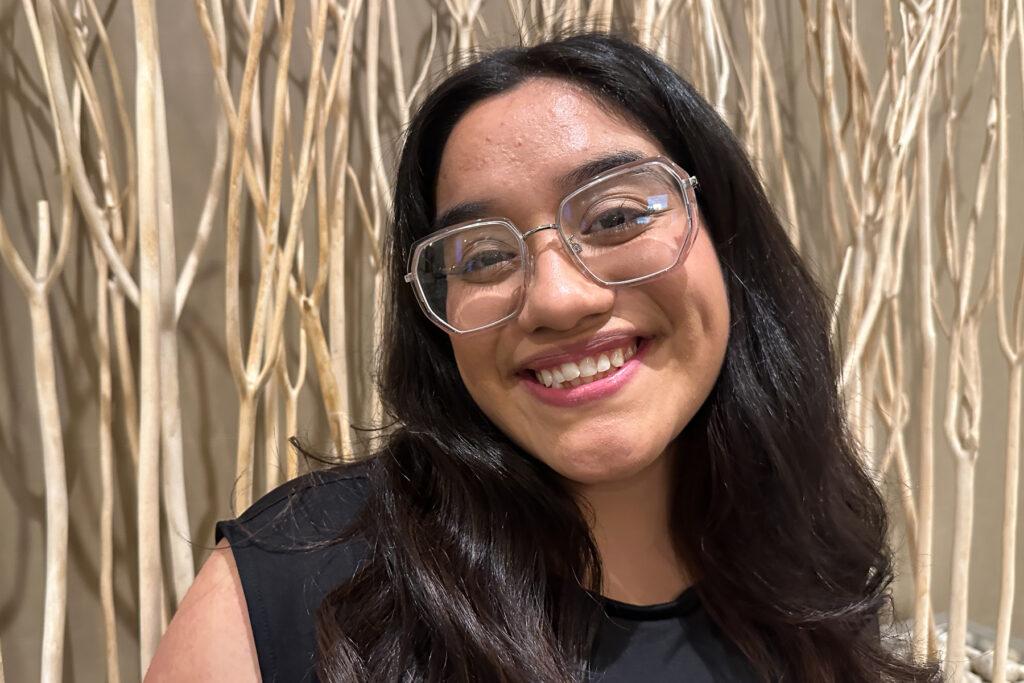 A close up portrait of a student with big clear glasses and a black shirt.