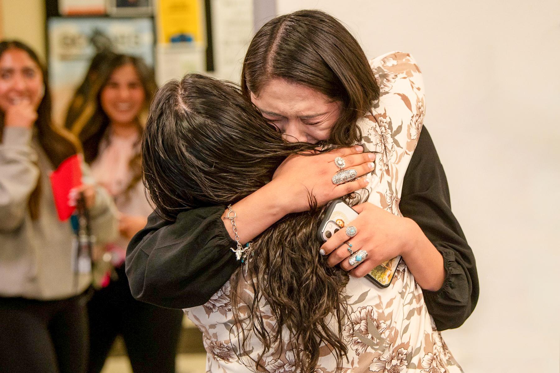 A student hugs a counselor and cries with her cell phone in her hand.