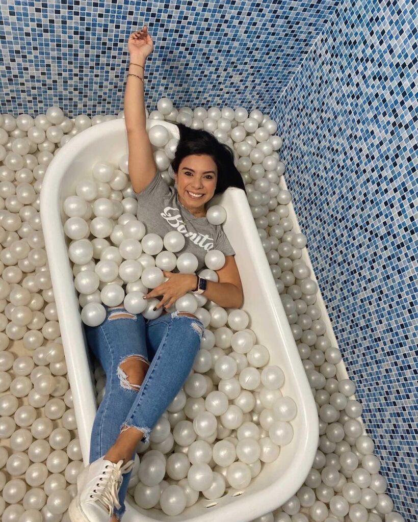 A woman sits in the bathtub with balloons made to look like bubbles, and then taking a selfie