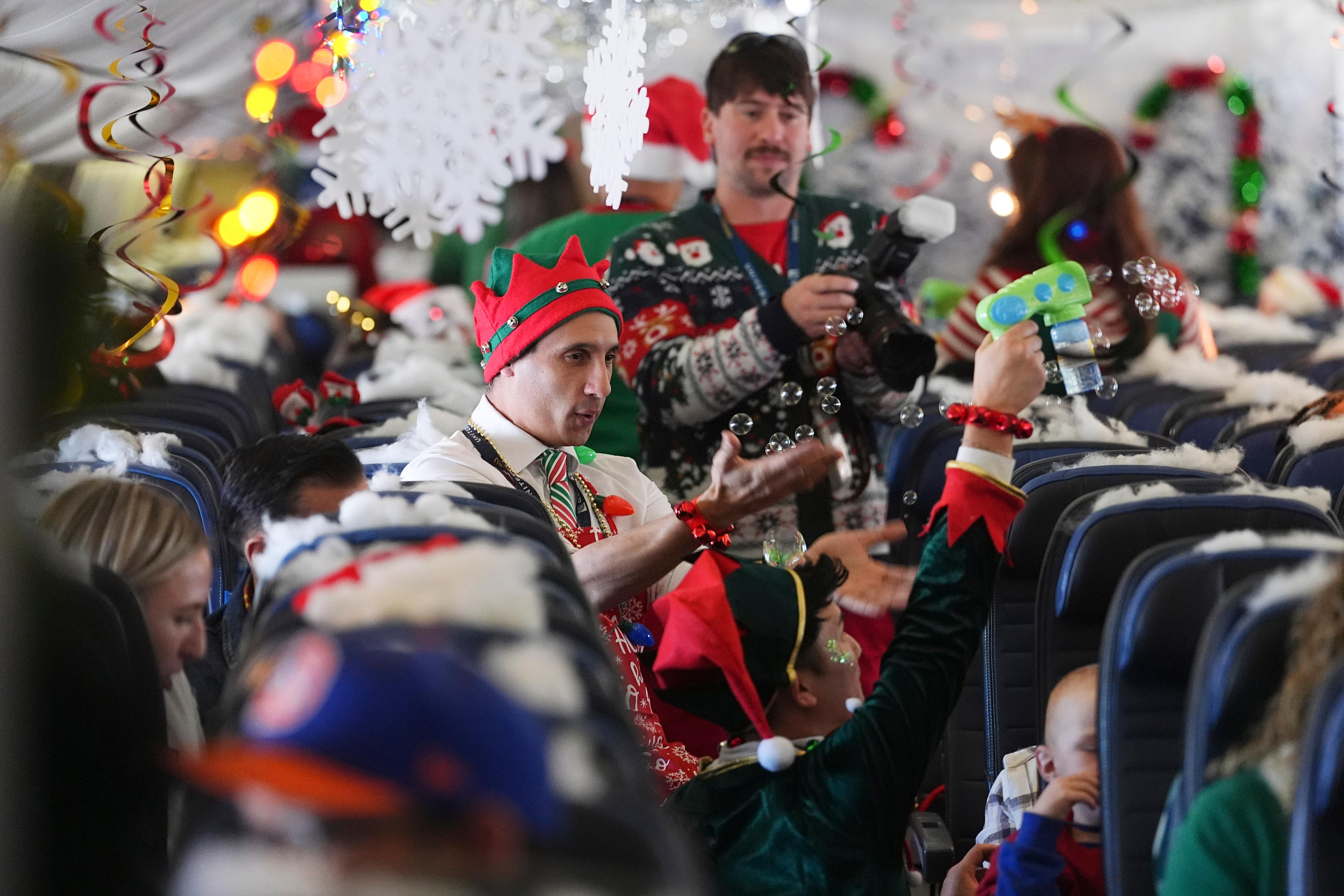 An airplane full of holiday decorations, with children and families packing the seats and flight attendants with elf hats and bubble guns roaming the aisle.