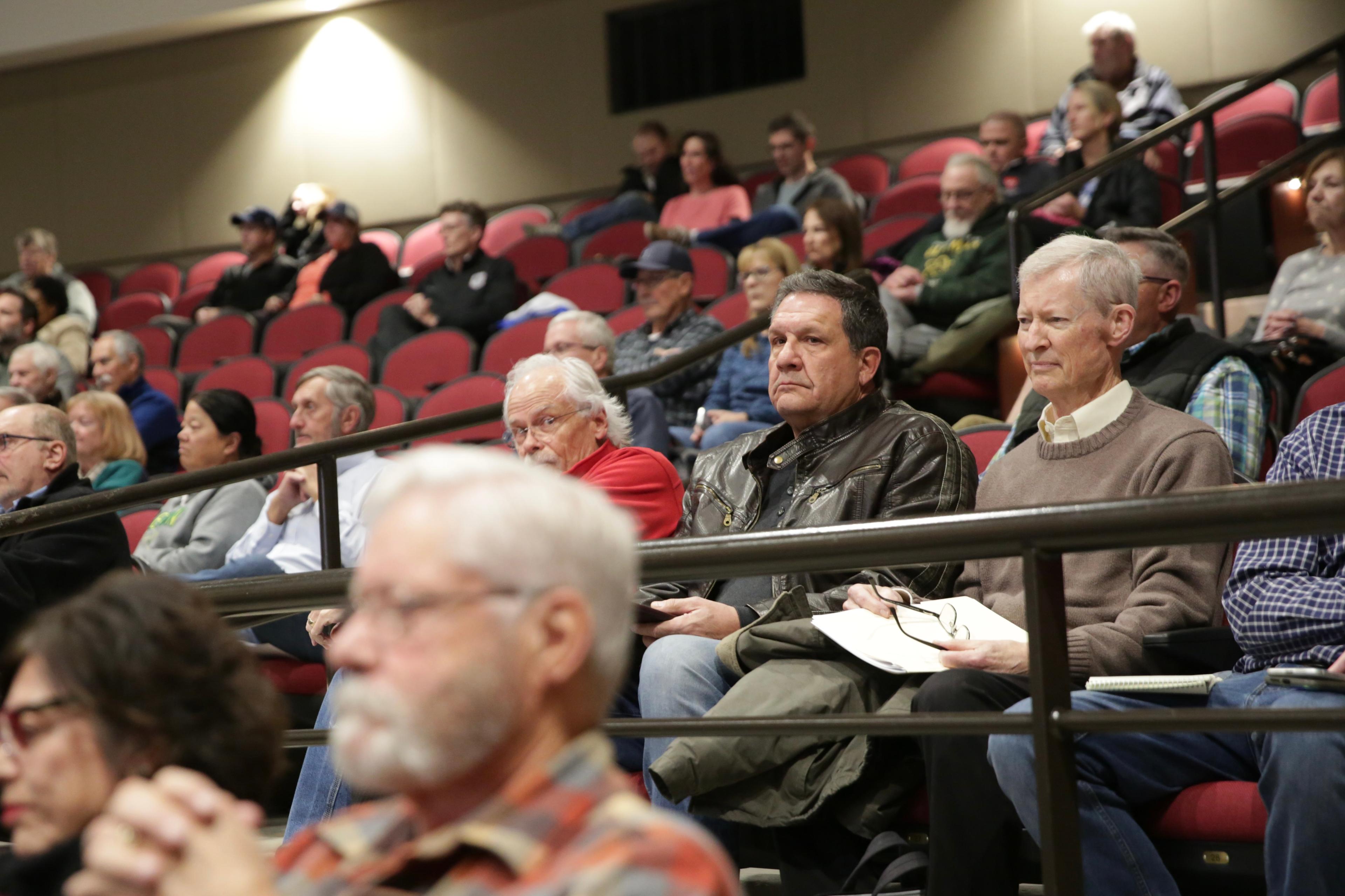 A man in a leather jacket sits amongst a theater audience