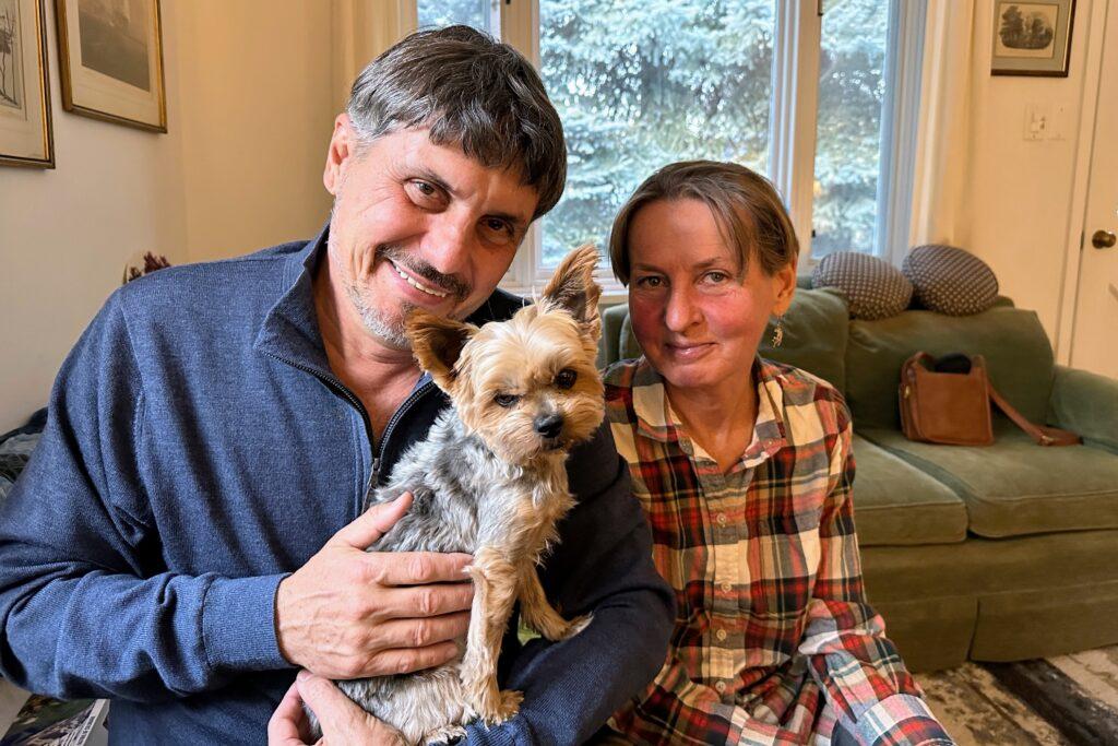 Artists Slava Leontyev and Anya Stasenko face the camera, while holding a small terrier dog.