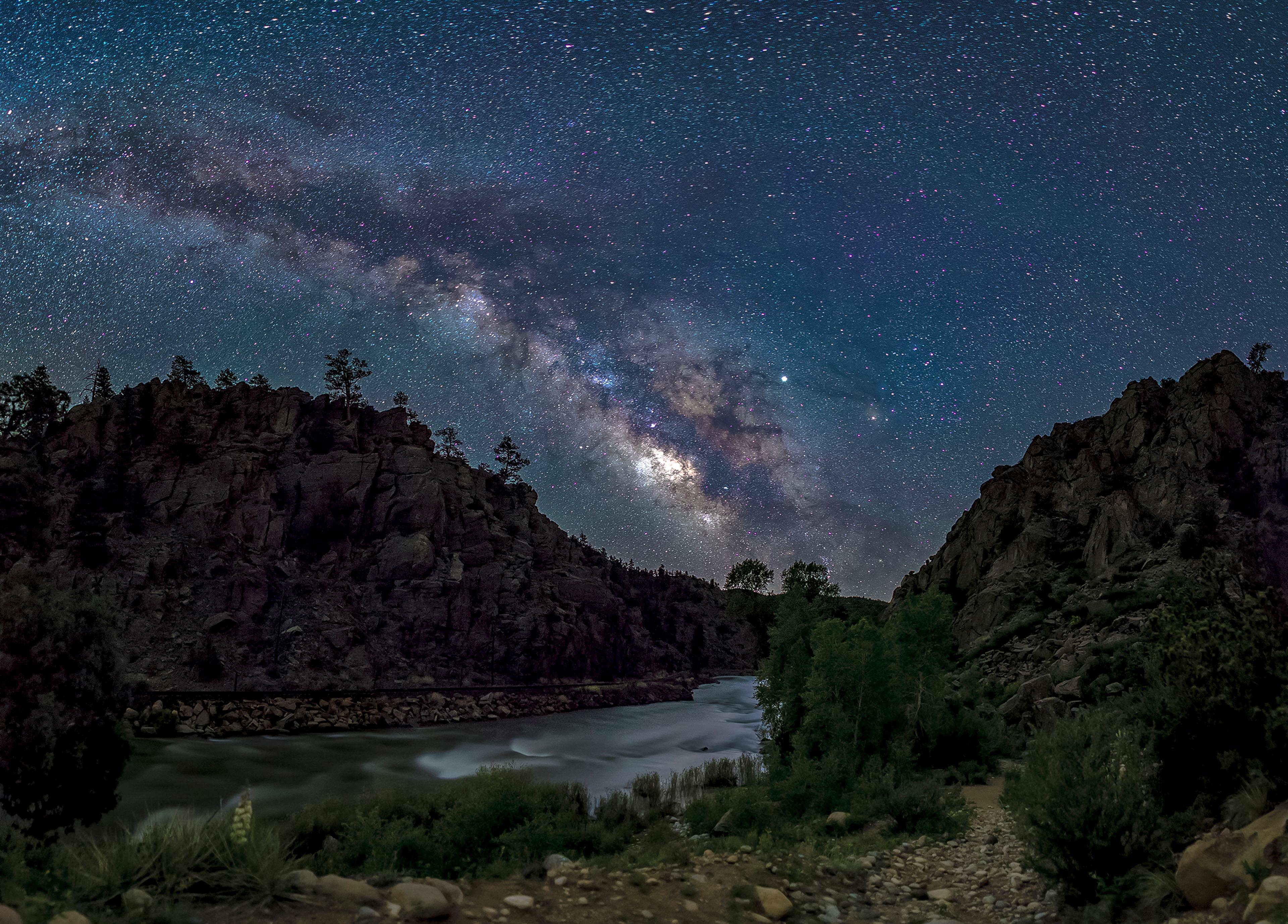 A starry night sky with the milky way stretching over Browns Canyon and the Arkansas River at night.