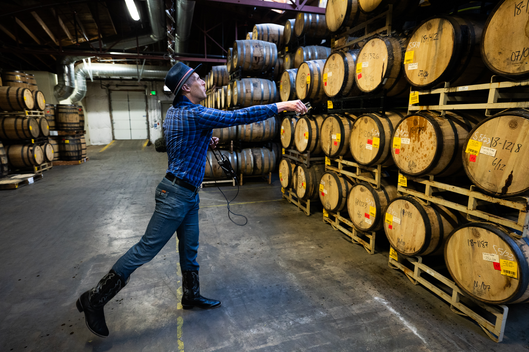 Ryan Warner throws a few drops of leftover whiskey at barrels in the rack room at Stranahan's distillery