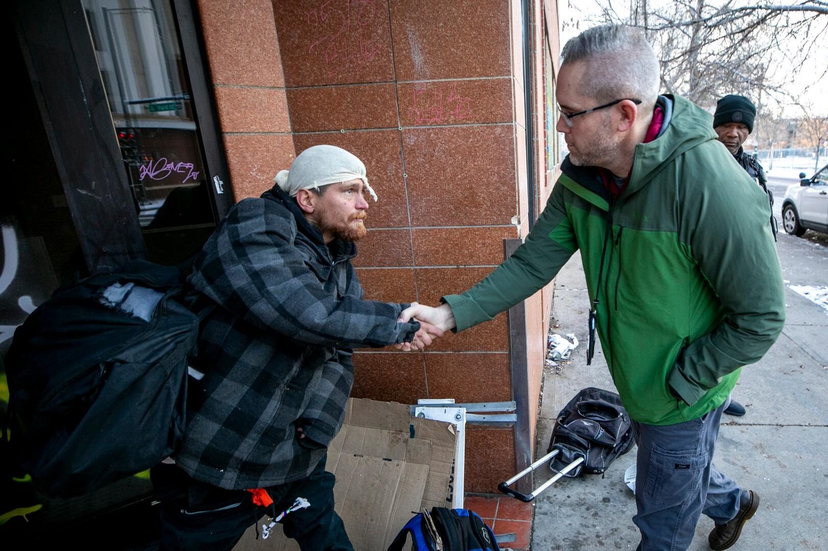 A man named Oliver, who said he slept outside last night, shakes hands with Chris Richardson, the Denver Police Department’s lead social worker, as Richardson picks him up to bring him to a local resource center. Dec. 10, 2024.