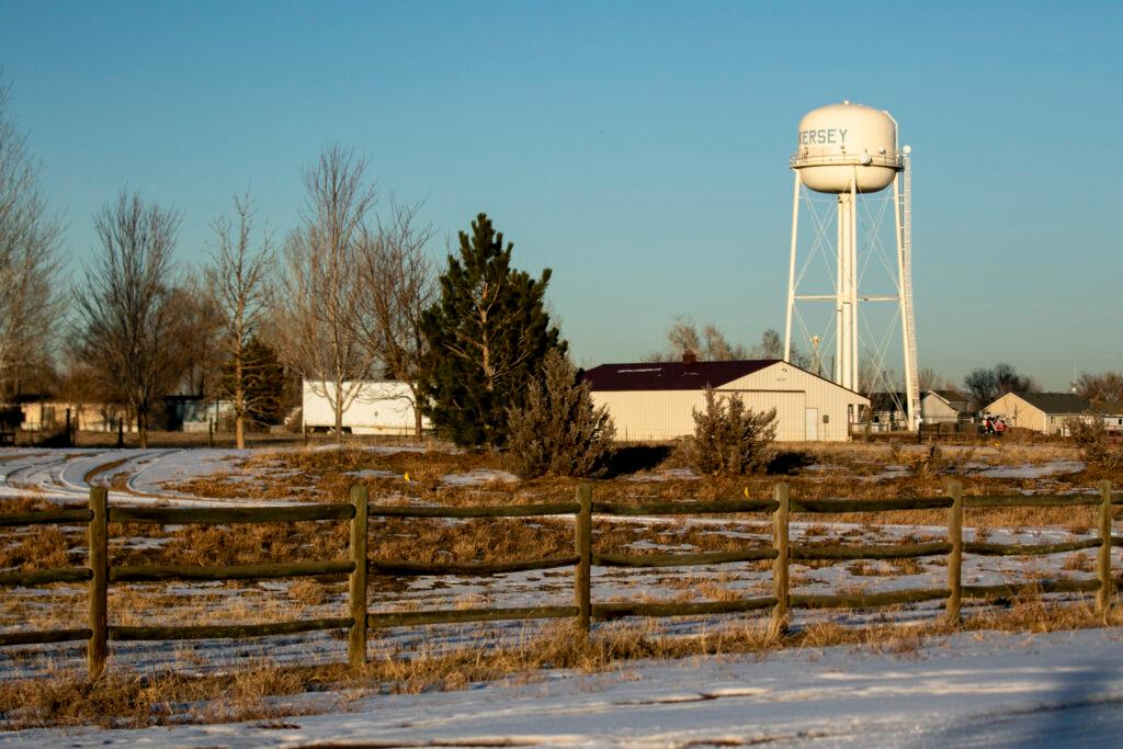 A large water tower stands in the background with houses and a wooden fence in the foreground.