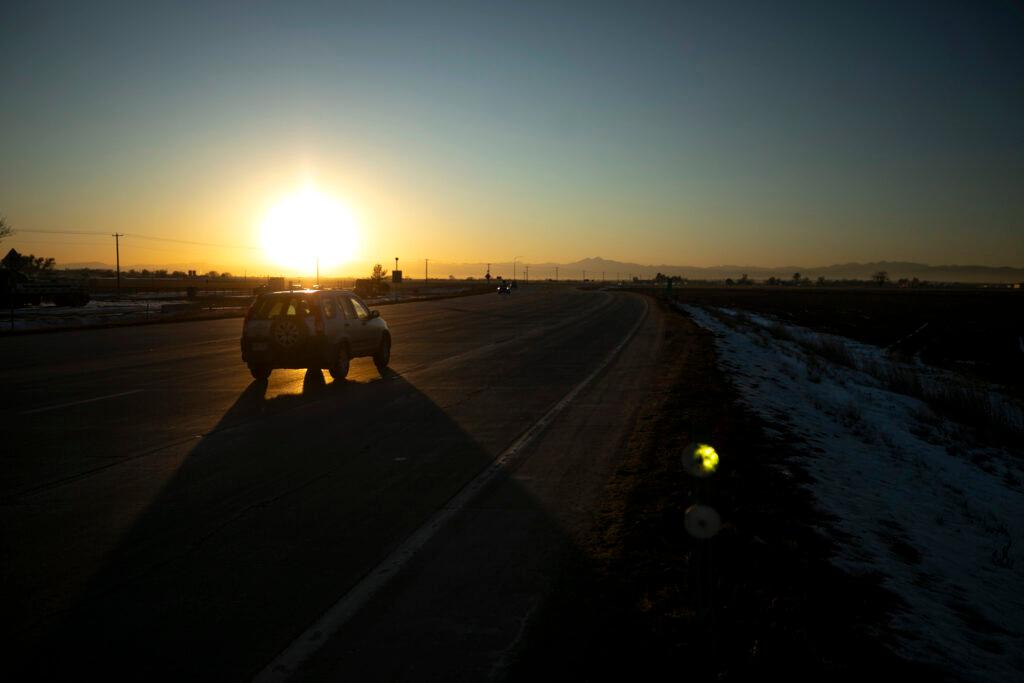 A car drives on a road near sunset with mountains in the far off background.